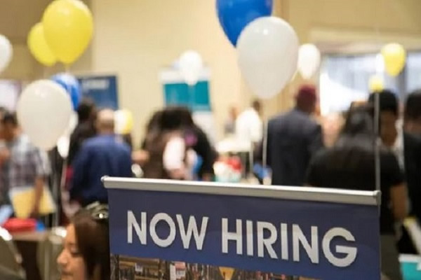 a now hiring sign in a room with people and balloons